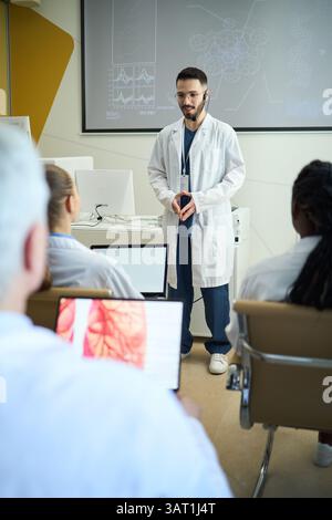 Formazione di un gruppo di studenti diversi in una moderna sala di laboratorio con schermi di presentazione e attrezzature di laboratorio in background, coinvolgendo gli studenti Foto Stock