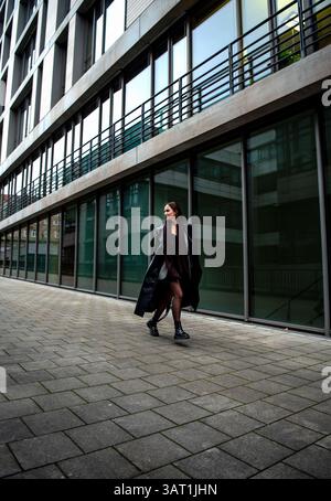 Elegante donna che corre e salta di fronte a un edificio di uffici a Stoccarda, Germania Foto Stock