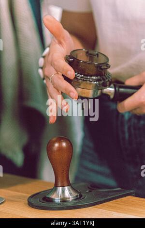 Primo piano delle mani che preparano il caffè macinato in un portafiltro su una macchina espresso in un ambiente bar. Foto Stock