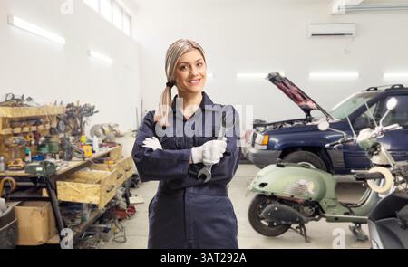 Lavoratrice meccanica di auto in uniforme che tiene una chiave in un garage Foto Stock