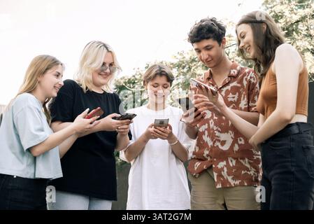 Gli adolescenti sorridono mentre utilizzano gli smartphone all'aperto Foto Stock