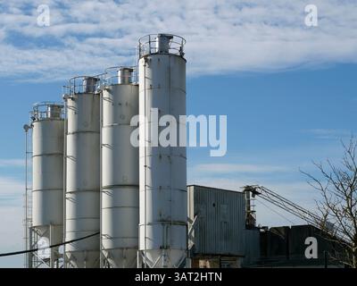 Più silos di una pianta di cemento si innalzano nel cielo. Impianto industriale in un'area commerciale, essenziale per i materiali da costruzione. Foto Stock