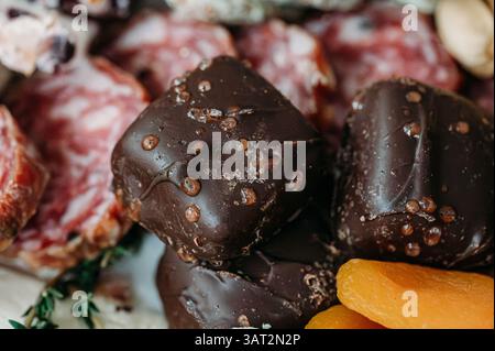 Primo piano di prelibatezze al cioccolato fondente accanto a salame e albicocche secche. Foto Stock