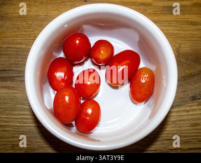 vista dall'alto dei pomodori rossi freschi disposti su uno sfondo rustico in legno. L'immagine evidenzia il colore vivace e la consistenza naturale dei pomodori, Foto Stock