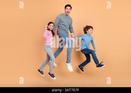 Allegra famiglia che salta insieme sullo sfondo beige celebrando felicità e legame Foto Stock