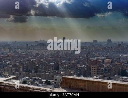 Una vista panoramica del Cairo, in Egitto, che mostra un vasto paesaggio urbano sotto un cielo spettacolare con raggi di luce del sole che si infrangono attraverso le nuvole. Gli iconi Foto Stock
