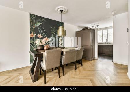 Un'elegante zona pranzo caratterizzata da un suggestivo murale botanico, mobili eleganti e caldo pavimento in legno, che creano un'atmosfera contemporanea e invitante. Foto Stock