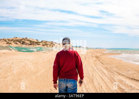 Fuoriuscita di olio combustibile. Un uomo cammina lungo una spiaggia sabbiosa con una duna di sabbia coperta da una rete protettiva di olio combustibile gettata sulla riva da un'onda. Foto Stock