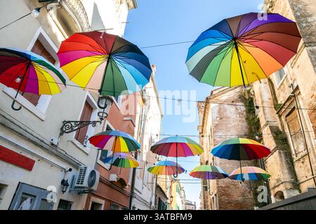 Ombrelli colorati appesi su una stretta strada di Chioggia, Italia, che creano una vivace e artistica scena urbana Foto Stock