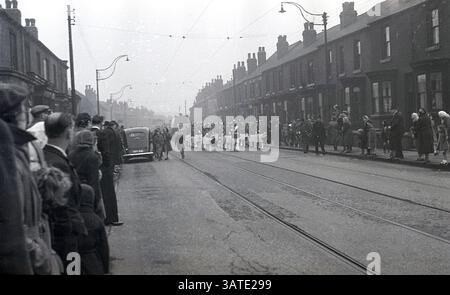 1950, storico carnevale di strada, persone in piedi ai lati di Staniford Road a Sheffield, Inghilterra, Regno Unito, guardando una band che conduce la processione. Foto Stock