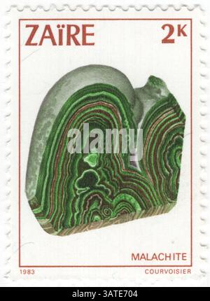 ZAIRE - 1983 febbraio 13: 2 makuta francobollo multicolore raffigurante Malachite, minerali di Zaire. La malachite è un minerale di idrossido di carbonato di rame, con la formula Cu2CO3(OH)2. Questo minerale opaco e a banda verde si cristallizza nel sistema cristallino monoclinico, e più spesso forma masse botrioidali, fibrose o stalagmiche, in fratture e spazi sotterranei profondi, dove la falda d'acqua e i fluidi idrotermali forniscono i mezzi per la precipitazione chimica. I singoli cristalli sono rari, ma si presentano come sottili prismi acicolari Foto Stock