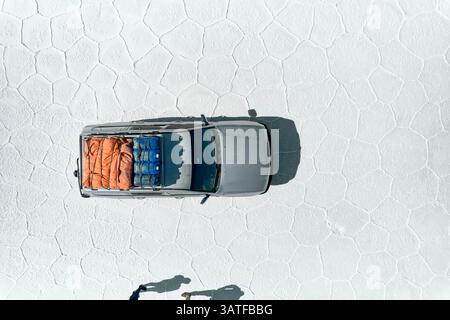 Vista aerea di un veicolo 4x4 con bagagli sui motivi geometrici esagonali salini di Salar de Uyuni. Auto con equipaggiamento da spedizione sul più grande salino del mondo Foto Stock