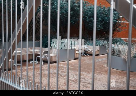 Londra, Regno Unito - 28 settembre 2024: Panchine e piantatrici in legno in un moderno giardino, viste attraverso barre verticali nella City di Londra. Foto Stock