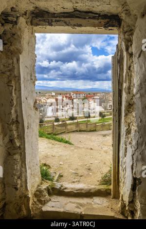 Le pareti sbriciolate di antiche grotte incorniciano la vista del villaggio di arguedas in navarra, spagna, sotto un cielo parzialmente nuvoloso Foto Stock