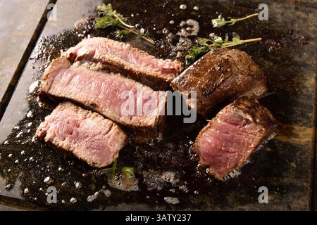 Deliziose bistecche di filetto di media rarità sfrigolano su una pietra calda, guarnite con timo fresco Foto Stock