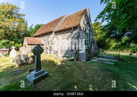 La chiesa normanna del XII secolo nel villaggio di Elmstone nel Kent. Esterno della nave e del Chancel costruito in selce con lapidi davanti. Cielo blu. Foto Stock