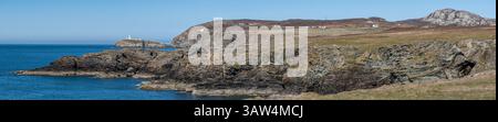 Panorama costiero a basso livello di mare aperto, faro di South Stack, scogliere circostanti e monte Holyhead sull'Isola di Anglesey, Galles del Nord Foto Stock