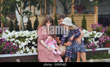 Genitori amorevoli che cullano la bambina appena nata accanto alla figlia maggiore in un giardino fiorito, condividendo teneri momenti in famiglia Foto Stock