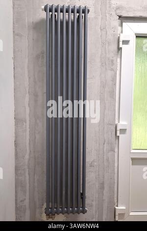 Radiatore metallico verticale su parete in cemento vicino alla porta Foto Stock