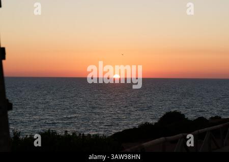 Splendido tramonto sulle calme acque oceaniche che creano un vivace cielo arancione e rosa Foto Stock
