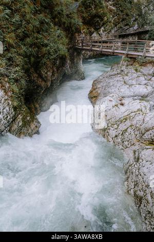 Le acque affollate si intagliano attraverso la stretta e rocciosa gola di Vintgar in Slovenia, incorniciata da passerelle in legno e scogliere mossy durante il freddo abbraccio dell'autunno Foto Stock