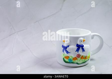Una tazza in ceramica bianca con due anatre è attualmente appoggiata su un tavolo Foto Stock