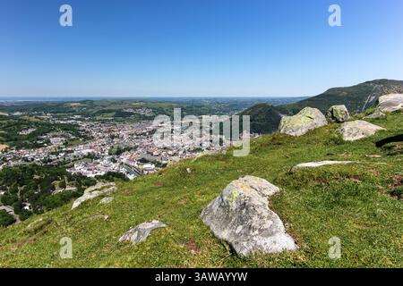 Città lontana annidata in una lussureggiante valle verde circondata da boschi e colline sotto un cielo azzurro. Gli elementi di rilievo includono paesaggi naturali e vegetazione Foto Stock