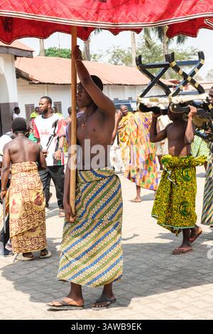 Kumasi, Ghana. Cerimonia Ashanti Akwasidae. I portatori portano un ombrello e una sedia per un capo locale. Foto Stock