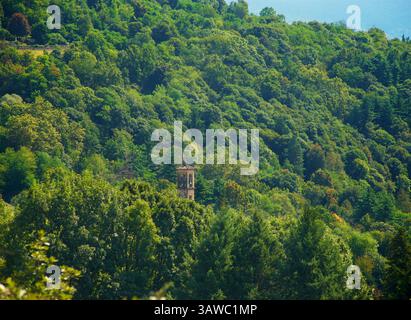 Il campanile di Chiesa Sant'Ambrogio, 21010 Montegrino Valtravaglia, provincia di Varese, Italia. Come si vede dal sentiero per la chiesa di San Martino. Il campanile di origine romanica, con finestre monofore lungo il pozzo e una successiva camera campanaria. Foto Stock