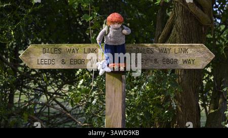 Yarnbomb persona attaccata al palo del dito (percorso pedonale pubblico a lunga distanza, collegamento Ebor Way, Dales Way) da vicino - Menston, West Yorkshire, Inghilterra Regno Unito. Foto Stock