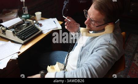 Ripresa cinematografica dell'autore alla scrivania d'epoca, che parla al telefono con una macchina da scrivere e documenti con una messa a fuoco morbida. Foto Stock