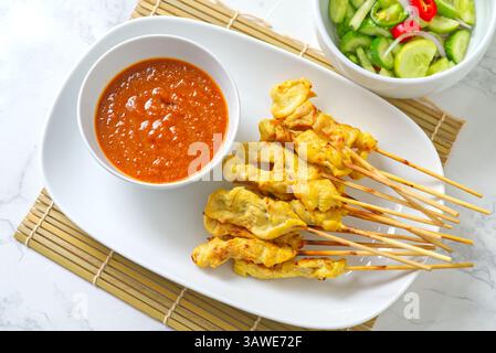 Moo Satay è uno spiedino di maiale alla griglia in stile thailandese con salsa di arachidi e insalata di cetrioli. Si tratta di uno spuntino tailandese con vista dall'alto servito su un piatto bianco su un bamb Foto Stock