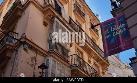 Vista ad angolo basso di un edificio residenziale con facciata decadente e balconi nel centro storico di Cadice, con un cartello commerciale appeso - CADICE, SPAGNA - MARZO Foto Stock