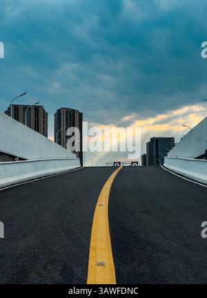 L'ampia autostrada si estende verso un cielo nuvoloso in un ambiente urbano moderno al tramonto Foto Stock