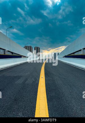 L'ampia autostrada si estende verso un cielo nuvoloso in un ambiente urbano moderno al tramonto Foto Stock