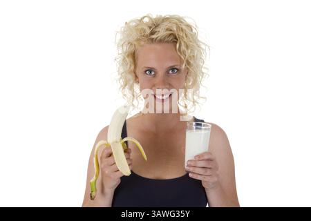 Giovane donna bionda che tiene in mano una banana e un bicchiere di latte giovane donna bionda che tiene una banana e un bicchiere di latte in mano Foto Stock