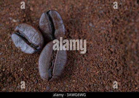 Primo piano di chicchi di caffè tostati su un letto di caffè appena macinato, che mostra la ricca consistenza e l'aroma di questa amata bevanda Foto Stock