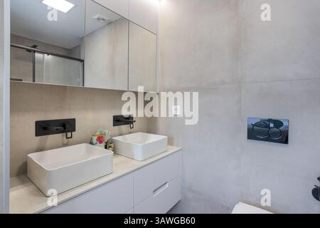 Bagno dal design elegante con doppio lavandino quadrato, finiture nere, grandi armadi a specchio e tessuti in pietra neutra. Foto Stock