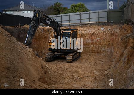 Escavatore cingolato giallo e nero Hyundai HX145LCR seduto in un buco su un cantiere suburbano, circondato da terra rossastra Foto Stock