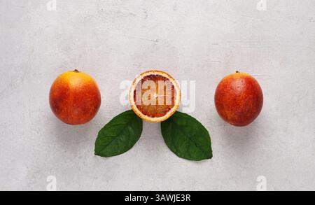 Arance sanguinose sullo sfondo in cemento, intere e a pezzi con foglie, vista dall'alto, spazio di copia Foto Stock