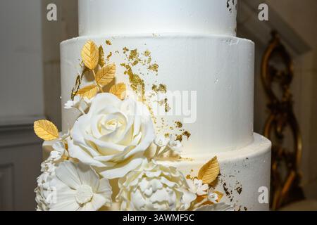 Primo piano di una torta nuziale con foglia d'oro e fiori di zucchero Foto Stock