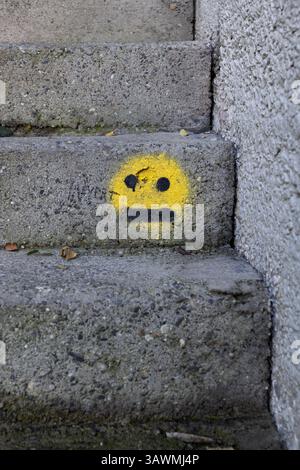 Emoji gialla su scale urbane in cemento, emoticon che mostra il volto neutro dritto, disinteressato, annoiato, nessuna espressione, indecisione, meh o senza espressioni Foto Stock