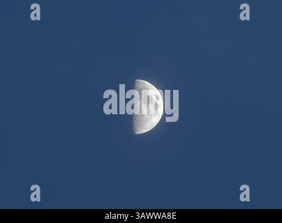 Primo quarto di luna visibile in un cielo azzurro e limpido sull'Italia. I dettagli della superficie e la transizione delle ombre sono chiaramente definiti in questo captur cielo minimalista Foto Stock