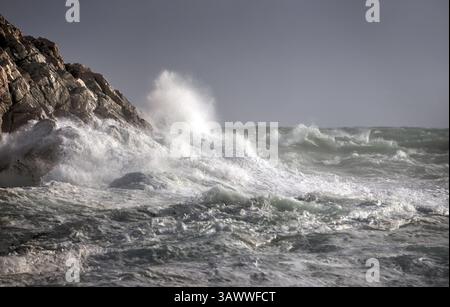Onde potenti si scontrano contro scogliere rocciose, catturando l'energia grezza e la bellezza dell'oceano durante una tempesta. Foto Stock