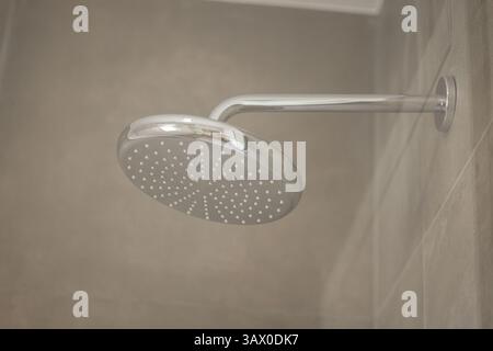 Una moderna doccia cromata con ugelli multipli è montata su una parete piastrellata del bagno, caratterizzata da un design elegante e piastrelle beige, per creare un ambiente pulito Foto Stock