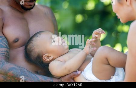 Felice bambino multirazziale. Bambino birazziale che giace sulle mani dei genitori. Padre e madre abbracciano un bambino birazziale. Padri e madri multirazziali mano per bambino Foto Stock