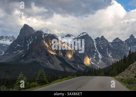 Una splendida catena montuosa con aspre cime torreggianti su una strada tortuosa. La luce del sole mette in risalto le rocce, mentre le nuvole sparse creano un cielo spettacolare Foto Stock