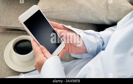 Donna che tiene o utilizza uno smartphone con una tazza di caffè nero su tessuto, NOMADE digitale, postazione di lavoro libera o concetto di shopping online Foto Stock