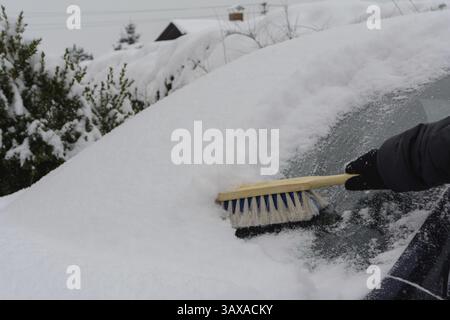 Il conducente di auto spazza il parabrezza innevato con una scopa da neve - primo piano Foto Stock