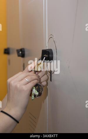 La persona apre l'armadietto - primo piano delle mani e lucchetto sull'armadietto metallico Foto Stock